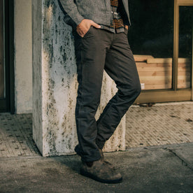 fit model leaning against pillar wearing The Morse Pant in Dark Charcoal Slub