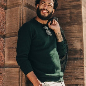 fit model wearing The Double Knit Sweater in Forest, leaning agains wall