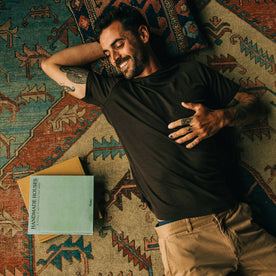 fit model wearing The Merino Tee in Heather Espresso, laying on ground next to books