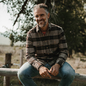 fit model wearing The Ledge Shirt in Espresso Plaid, sitting on fence