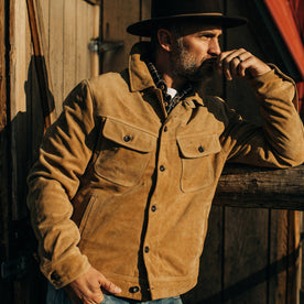 fit model wearing The Lined Long Haul Jacket in Sand Suede in front of a barn