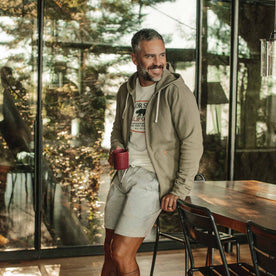 our fit model wearing The Après Hoodie in Olive—holding coffee, looking left