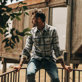 fit model wearing The Ledge Shirt in Navy Plaid, sitting on railing