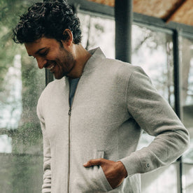 our fit model wearing The Heavy Bag Bomber in Heather Grey Fleece smiling while looking down with hand in pocket from the front