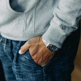 our fit model wearing The Heavy Bag Hoodie in Heather Grey Fleece with right hand in pocket showcasing TS embroidered logo on cuff