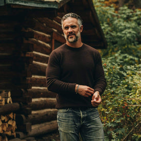 our fit model wearing The Lodge Sweater in Chocolate—near a cabin