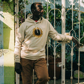 fit model leaning against fence wearing The Fillmore Hoodie in Sunflower Embroidery