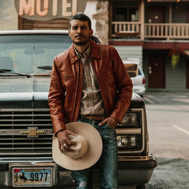 fit model wearing The Moto Jacket in Whiskey Steerhide, holding hat looking into camera