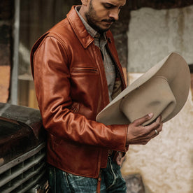 fit model wearing The Moto Jacket in Whiskey Steerhide, looking at hat