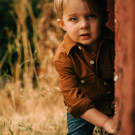 our fit model wearing The Little Yosemite Shirt in Tobacco—kneeling near a barn