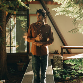 our fit model wearing The Yosemite Shirt in Tobacco—walking near a house in the woods